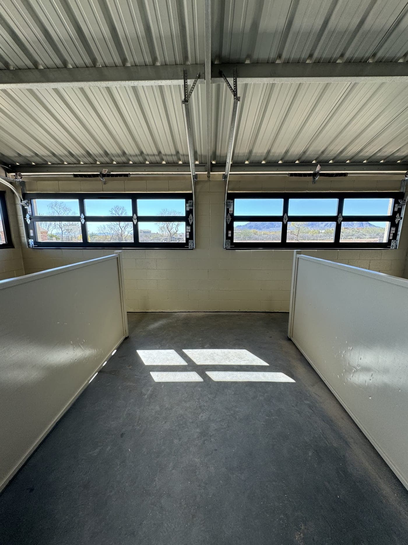 Two custom half-height glass garage doors installed in a stable track room, opened to the view