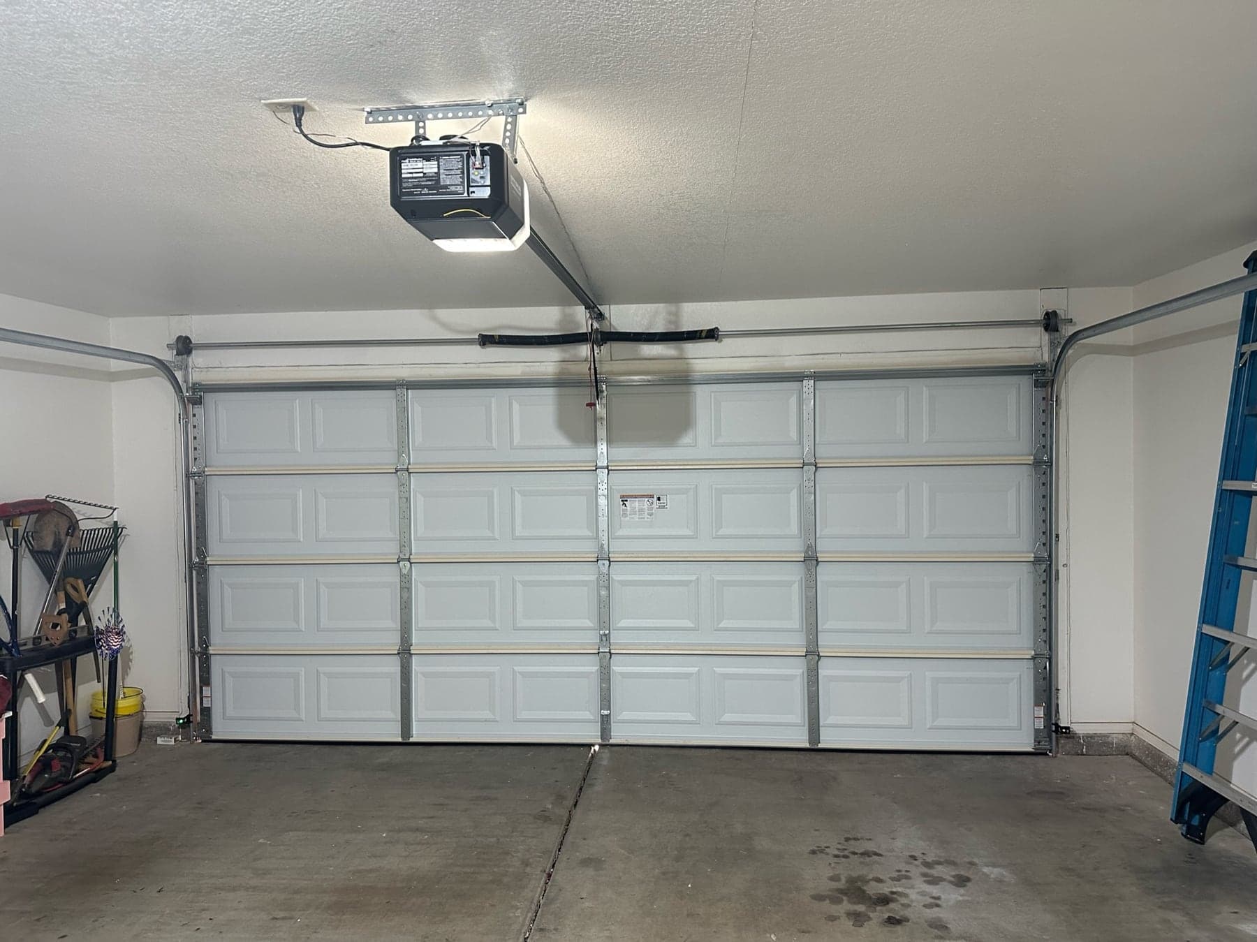 The inside of a garage door showing where each part sits: opener, springs, cables, rollers, tracks, panels and the bottom weather seal